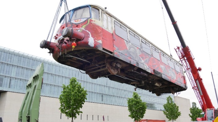 Maxvorstadt: Zwei Kräne setzen den alten Zugwaggon auf seiner neuen Wirkungsstätte ab.