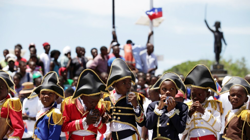 Children drink water before participate in a performance during the anniversary celebrations of Haiti's National flag day in Arcahaie, Haiti