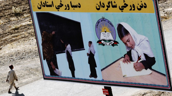 An Afghan boy walks past a billboard encouraging girls to go to school in Kandahar City