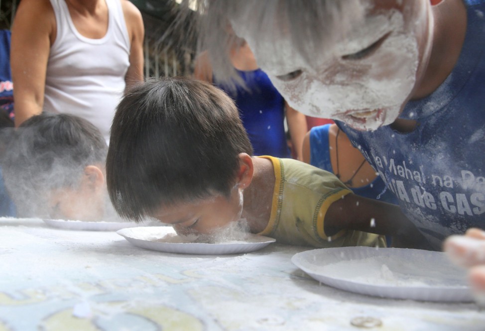Boys use their mouth to get coins in plates with flour during a game held at a town fiesta in celebration of the patron saint Santa Rita de Cascia in Baclaran