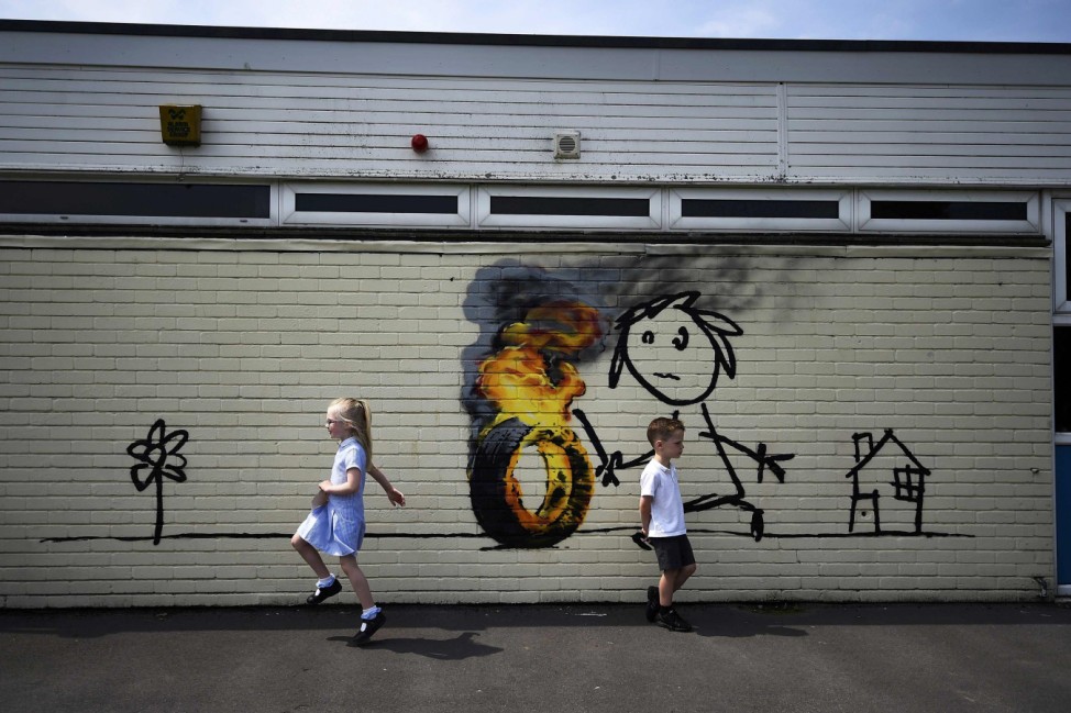 Reception class school children skip past a mural attributed to Banksy in Bristol