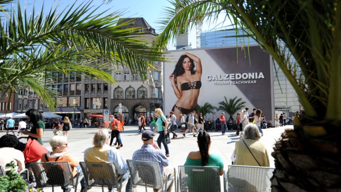 Werbung: Seit Dienstag ist die Werbung am Marienplatz etwas von Topfpalmen bedeckt. Manche Flaneure und Touristen beachten sie kaum, andere machen Selfies.