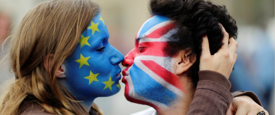 Two activists with the EU flag and Union Jack painted on their faces kiss each other in front of Brandenburg Gate to protest against Brexit in Berlin