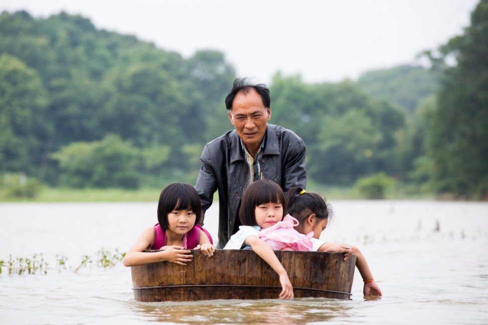 A man pushes a tub carrying children as he gets them back home after school at a flooded area in Duchang