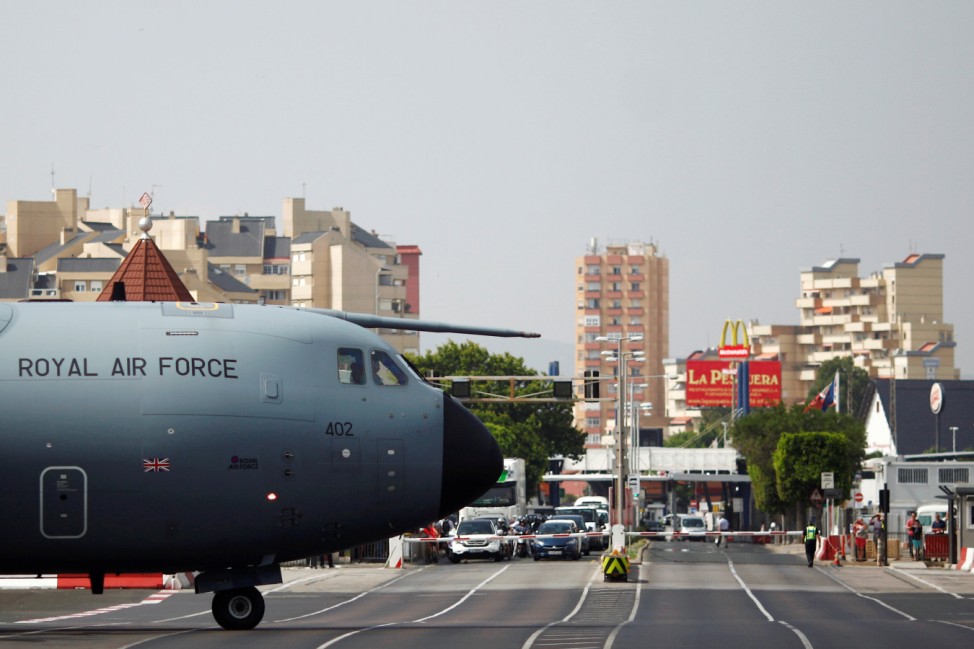 Pedestrians and drivers wait to cross the road of the Gibraltar International Airport as a British Royal Air Force plane taxis on the tarmac after landing in the British overseas territory of Gibraltar