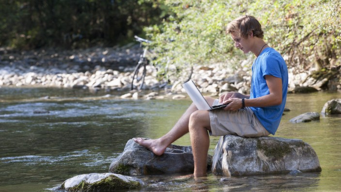 Austria Salzkammergut Mondsee young man with laptop learning at a brook model released PUBLICATIO