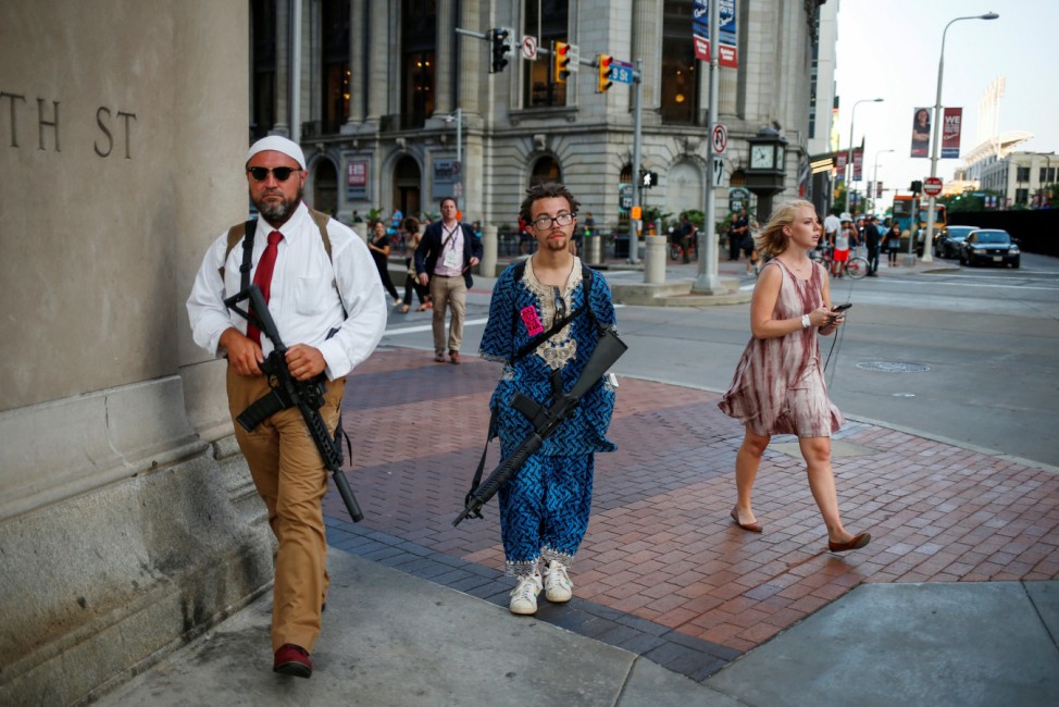 A woman walks past Micah Naziri and Jaimes Campbell, advocates for open carry, as they patrol the streets of Cleveland with their assault weapons during the Republican National Convention in Ohio