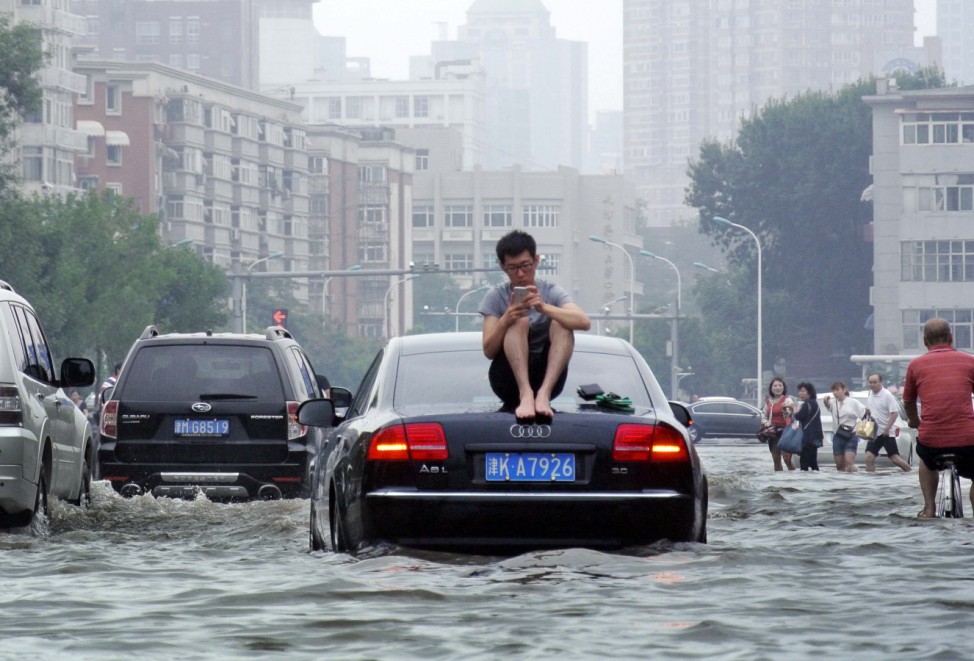 A man sits on top of a car as he is stranded on a flooded street in Tianjin