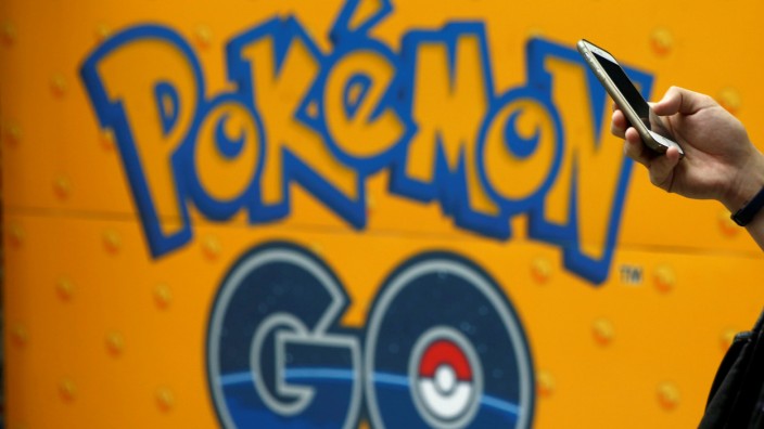 A man uses a mobile phone in front of an advertisement board bearing the image of Pokemon Go at an electronic shop in Tokyo