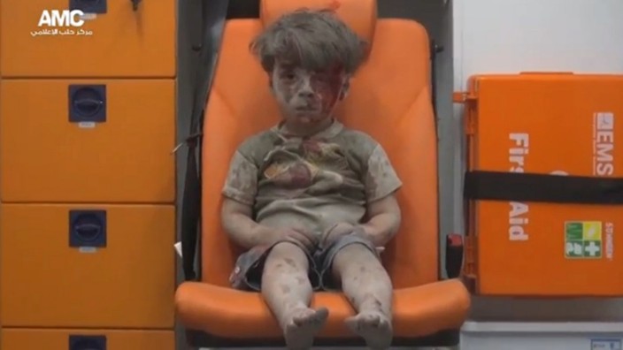 A still image from a video posted on social media shows a boy with bloodied face sitting in an ambulance, after an airstrike