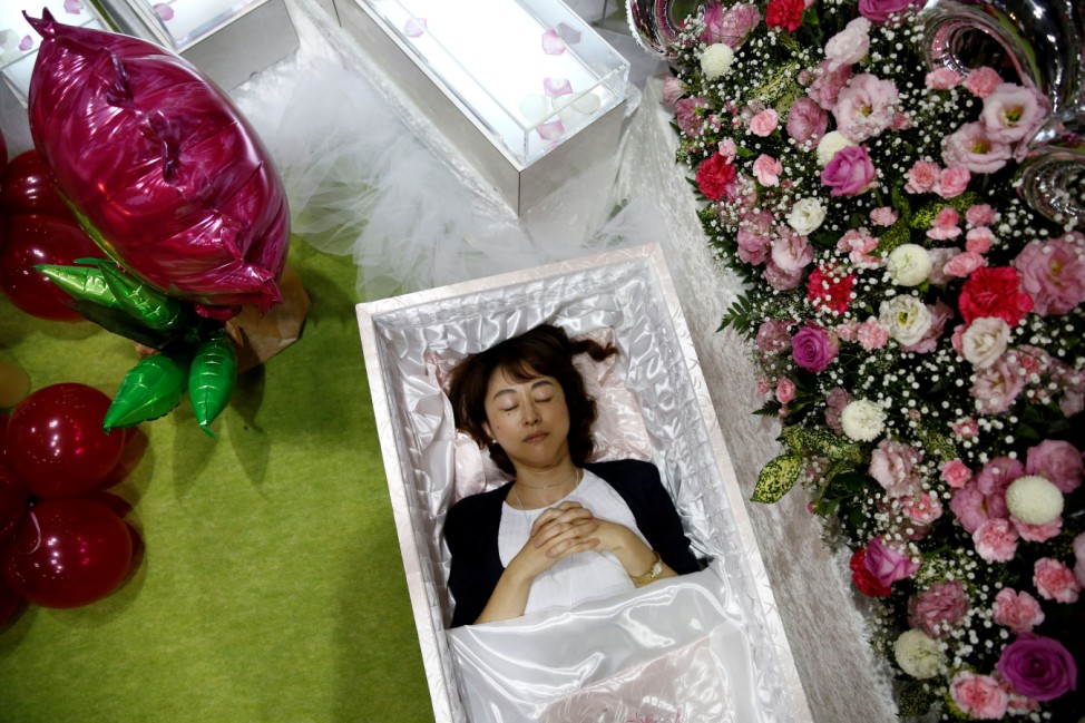 A staff lies in a casket next an altar decorated with flowers and balloons as she demonstrates Okuribito funeral's funeral service at the Life Ending Industry Expo in Tokyo