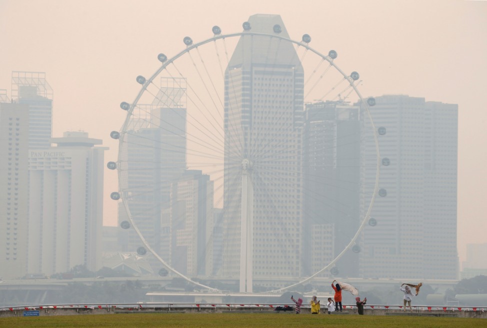 People take photos near the Singapore Flyer observatory wheel shrouded by haze