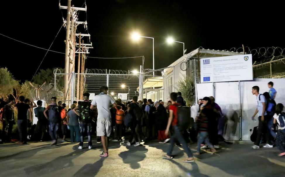 Refugees and migrants stand at the closed gate of the Moria migrant camp, after a fire at the facility, on the island of Lesbos
