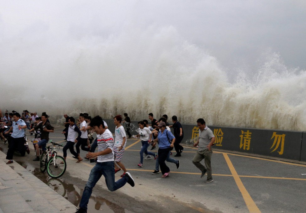 People run way from waves caused by a tidal bore which surged past a barrier on the banks of Qiantang River, in Hangzhou