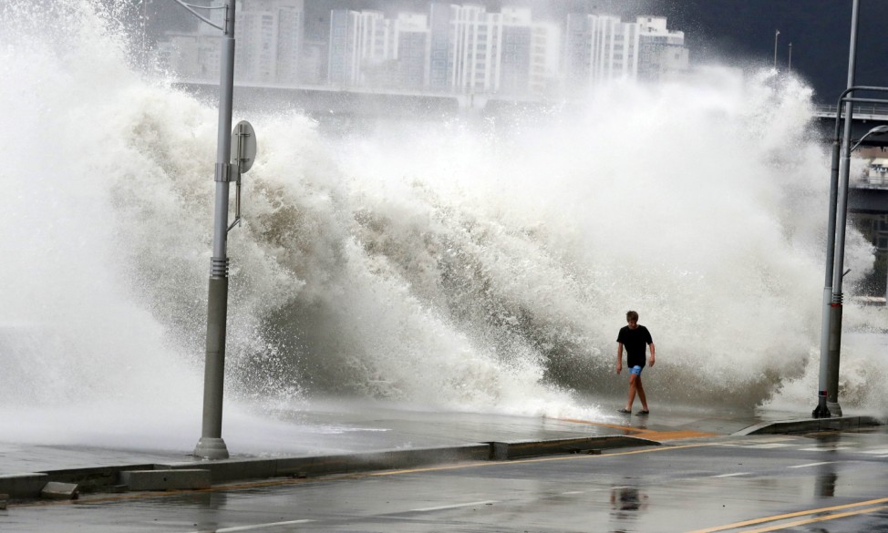 A man walks as a wave caused by typhoon Chaba splashes a seawall in Busan