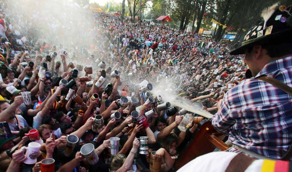 Visitors try to fill their mugs as beer is sprayed on them from a barrel at Argentina's Oktoberfest in Villa General Belgrano, Argentina