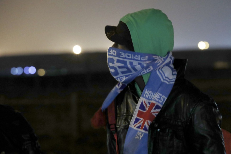 A migrant wears a soccer fan scarf as he queues for his evacuation and transfer to a reception center in France, and the dismantlement of the camp called the 'Jungle' in Calais starts