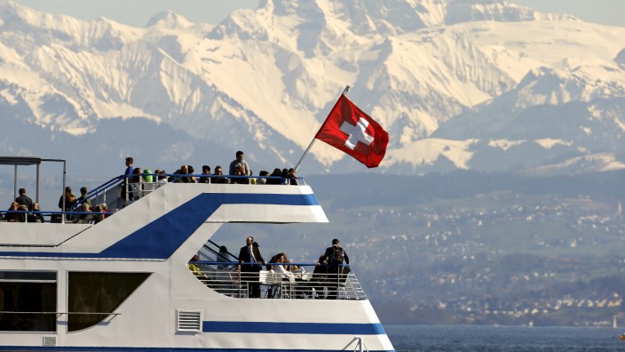 People enjoy the sunny spring weather aboard a tourist vessel sailing in front of the eastern Swiss Alps on Lake Zurich