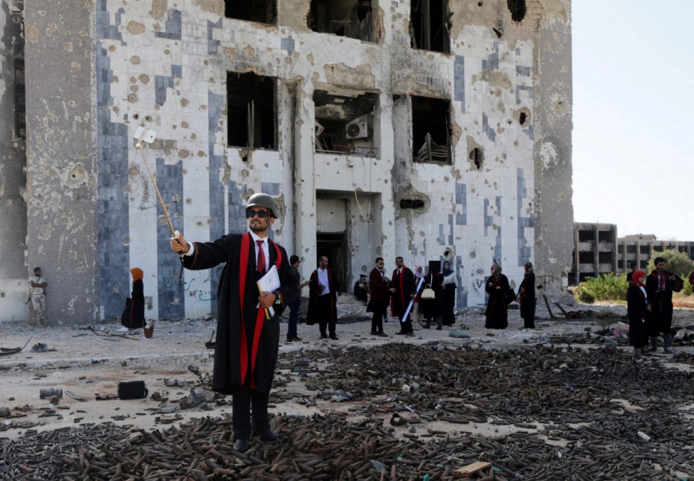 New graduate of Benghazi University takes a selfie in front of a ruined building at his university former headquarters in Benghazi