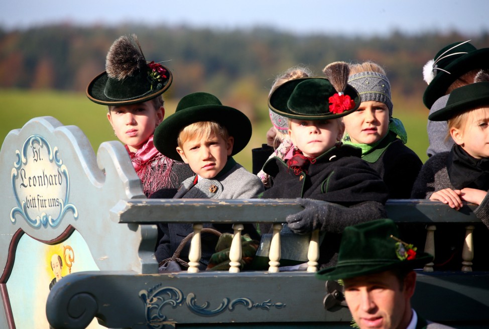 Farmers' children dressed in traditional Bavarian costumes ride in a wooden carriage on the way to the church of Reitham
