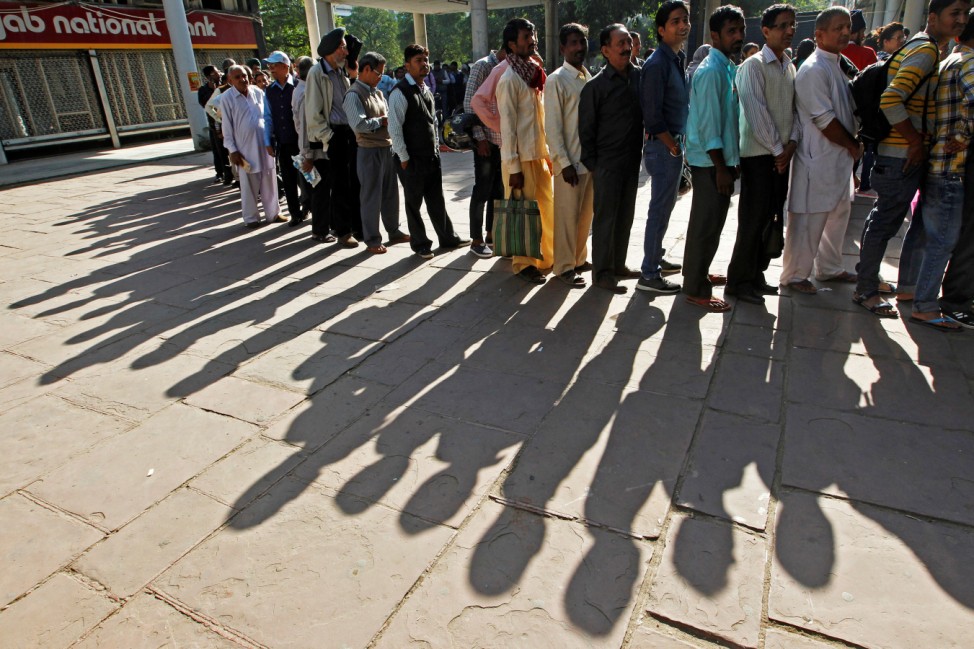 People cast their shadows on the ground as they queue to exchange their old high denomination banknotes outside a bank in Chandigarh