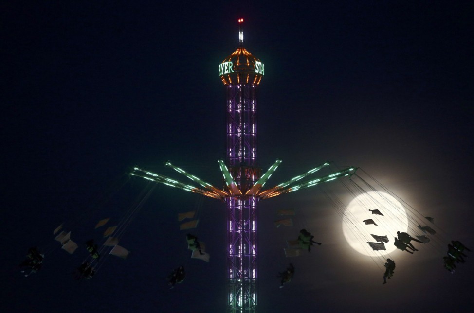 People on a funfair ride are silhouetted against the moon a day before the 'supermoon' spectacle, in London