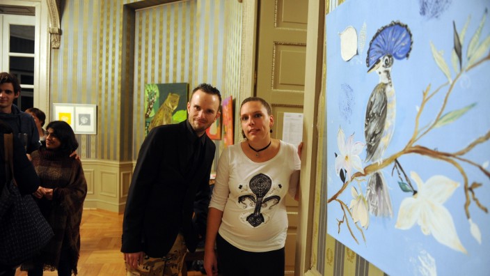 Ismaning: Andreas Uffinger stellt sich neben Veronika Hesse und deren Pfauenbild. Es ist eine Collage, die zu den exotisch-tierischen Motiven der Ausstellung in den mondänen Räumen des Schlosspavillons passt.