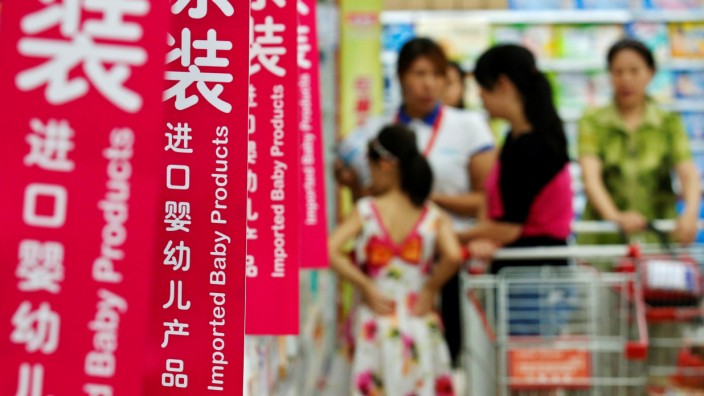 Customers talk to a sales assistant as they shop for milk powder in front of shelves displaying imported baby products at a supermarket in Beijing
