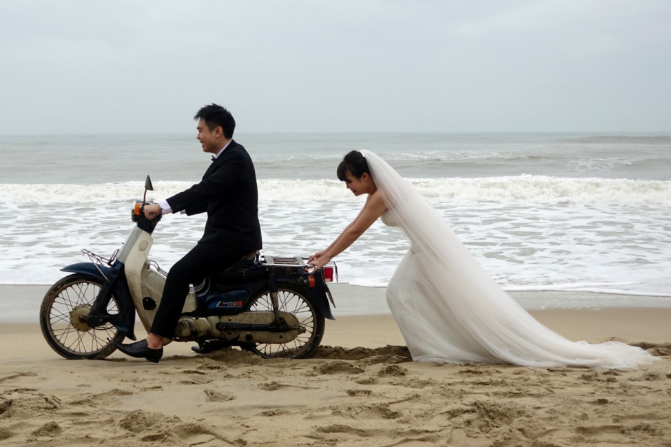 A Vietnamese bride is seen pushing the groom on a scooter during a photo shoot for their wedding in An Bang Beach outside Hoi An in Vietnam
