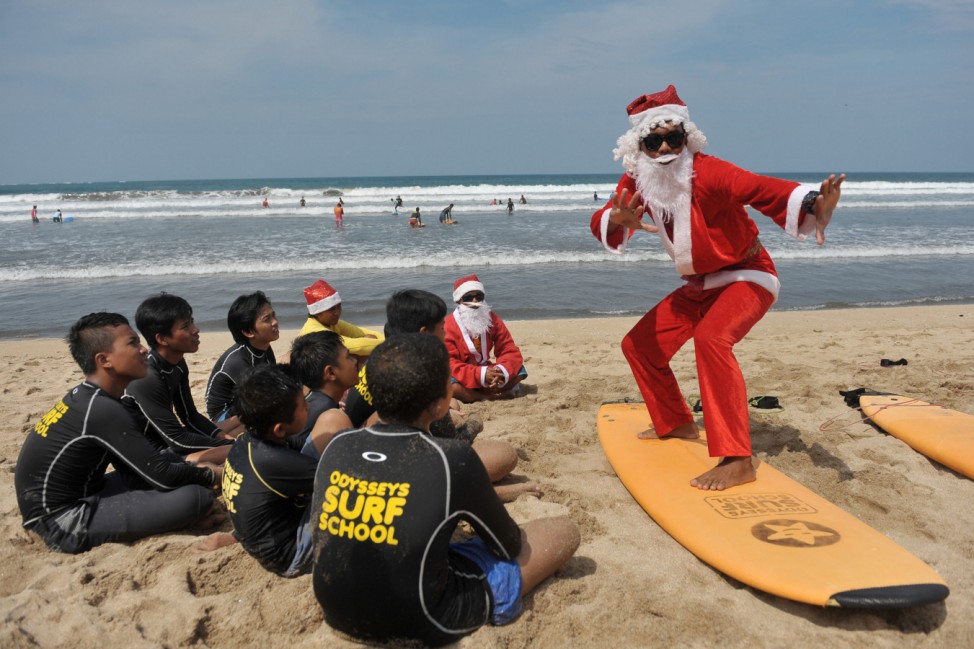 A surfing instructor dressed as Santa Claus gives a lesson to orphans on Kuta Beach