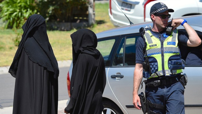 Women stand next to a policeman blocking a road where police officers are searching a house in the Melbourne suburb of Meadow Heights, Australia