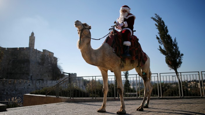 Kassissieh wears a Santa Claus costume as he rides a camel during an annual Christmas tree distribution by the Jerusalem municipality, in Jerusalem's Old City