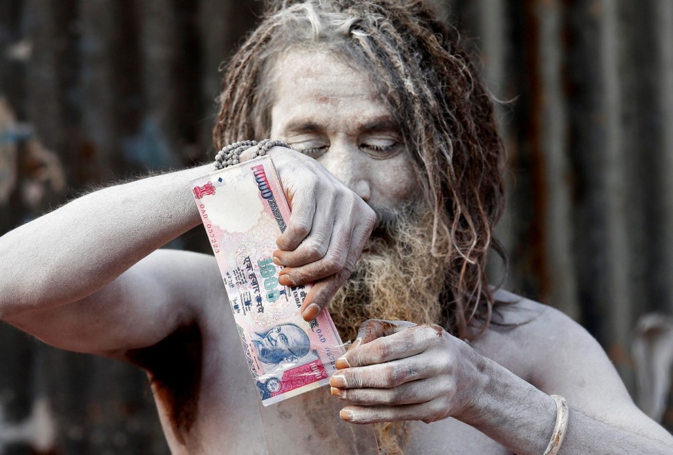 A Sadhu with his face covered with ash puts a wallet decorated with a print of the scrapped Indian 1000-rupee note inside a plastic cover at a makeshift shelter in Kolkata