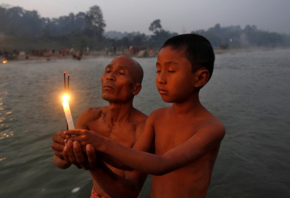 A Hindu man and his son hold burning incense sticks and a candle as they pray after taking a dip in the waters of river Howrah on the occasion of 'Makar Sankranti' festival in Chakmaghat village