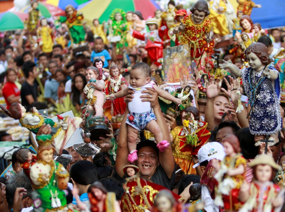 A devotee carries his child to be blessed by the lay minister with holy water during the annual feast of Sto. Nino in Manila