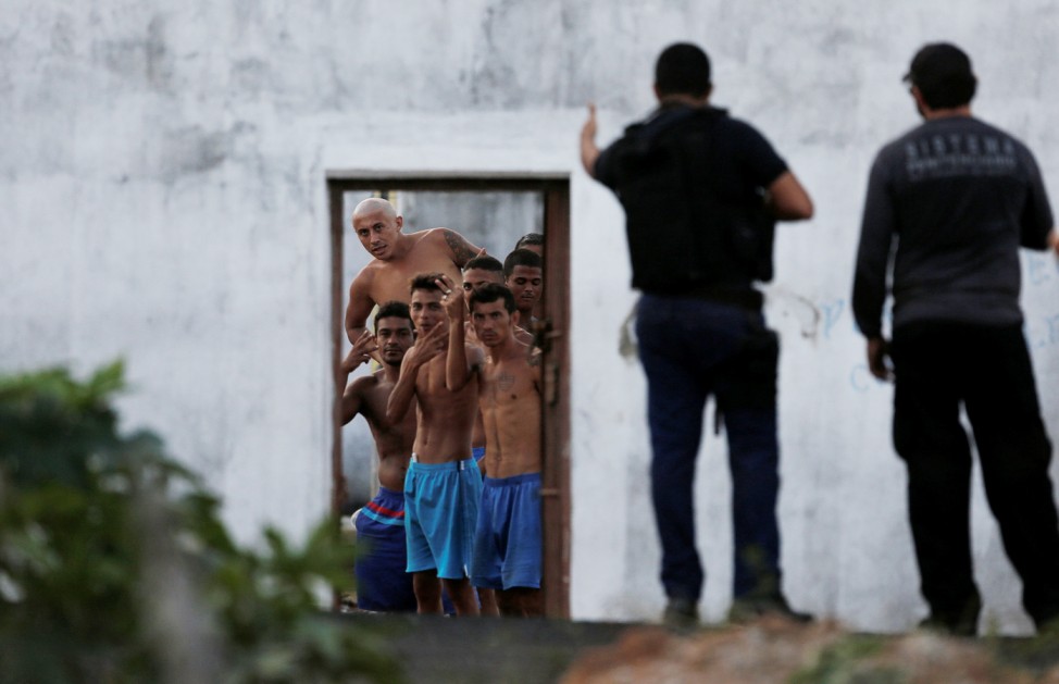 Inmates gesture in front of police officers after they delivered meals to them during an uprising at Alcacuz prison in Natal