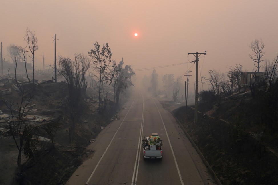 People ride in a car loaded with household items as they drive past burnt houses as the worst wildfires in Chile's modern history ravage wide swaths of the country's central-south regions, in Santa Olga