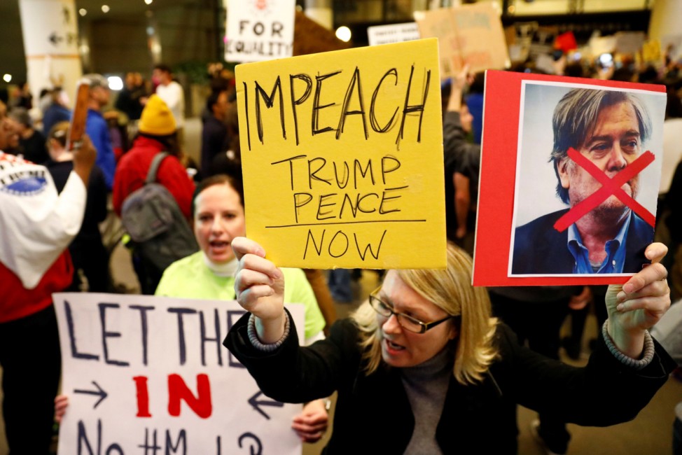 A woman holds signs against Steve Bannon and encouraging the impeachment of Trump and Pence during a protest of Donald Trump's travel ban from Muslim majority countries at the International terminal at Los Angeles International Airport (LAX) in Los Angele
