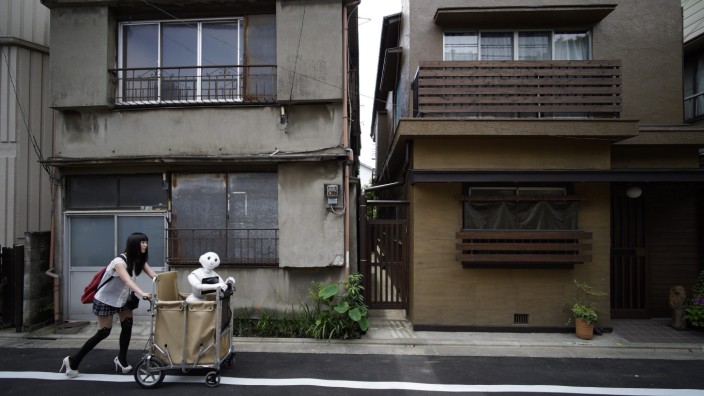 Mensch und Maschine: Tokio zwischen Tradition und Moderne: Eine junge Frau kutschiert ihren Roboter an heruntergekommenen Wohnhäusern vorbei.
