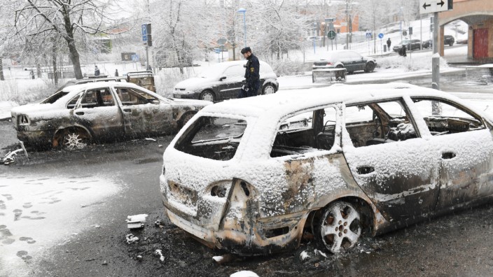 A policeman investigates a burnt car in the Rinkeby suburb outside Stockholm