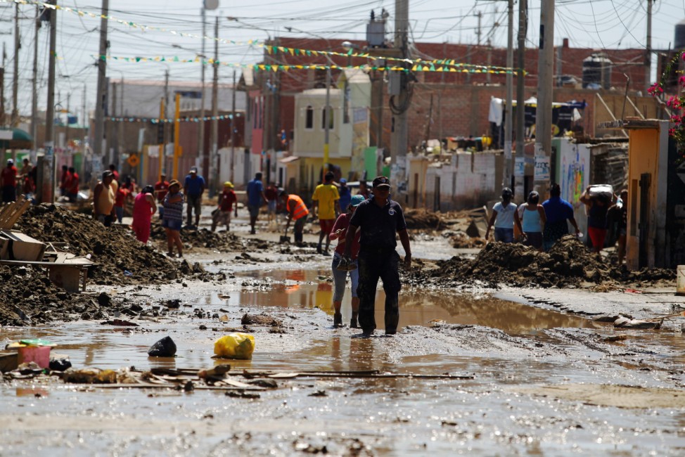People are seen at a flooded street, after rivers breached their banks due to torrential rains, causing flooding and widespread destruction in Huarmey.