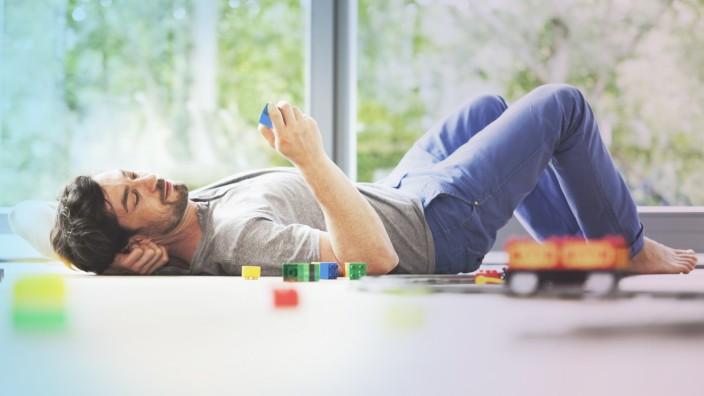 Man lying on floor with cell phone next to toy train model released Symbolfoto property released PUB