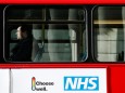 FILE PHOTO:  A man sits on a bus with an advertisement for Britain's National Health Service (NHS) in London
