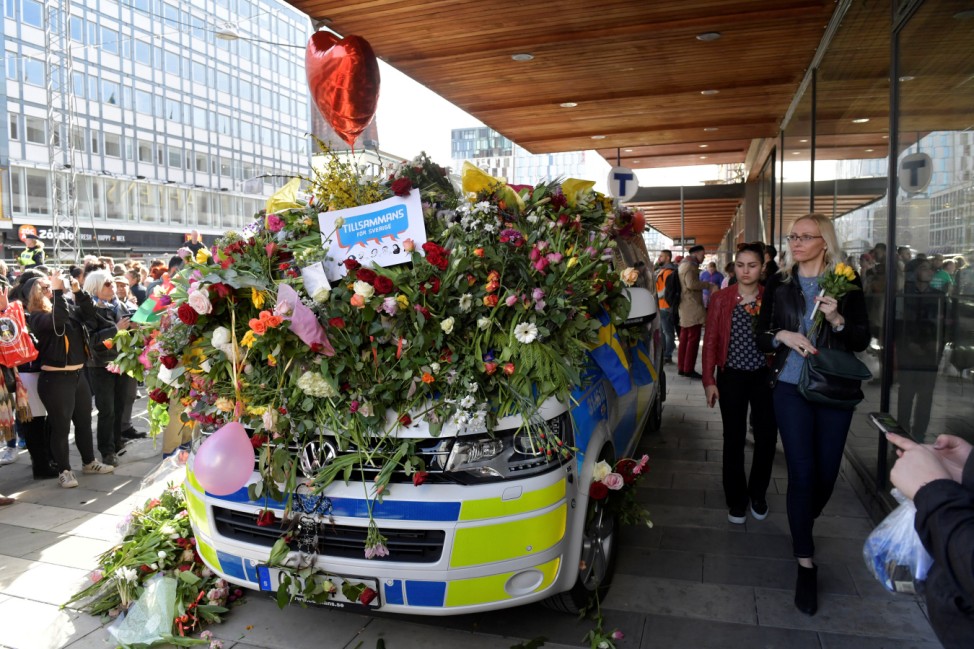 People put flowers on a police vehicle outside Ahlens department store, following Friday's attack, in central Stockholm