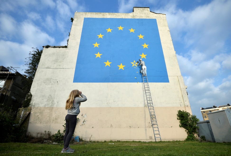 A young girl looks at artwork attributed to street artist Banksy, depicting a workman chipping away at one of the 12 stars on the European Union, seen on a wall in the ferry port of Dover