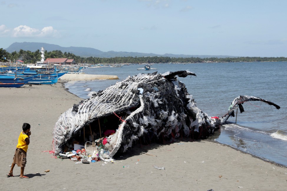 A boy looks at a whale shaped art installation that is made of plastic and trash made by environmental activist group Greenpeace Philippines in Cavite