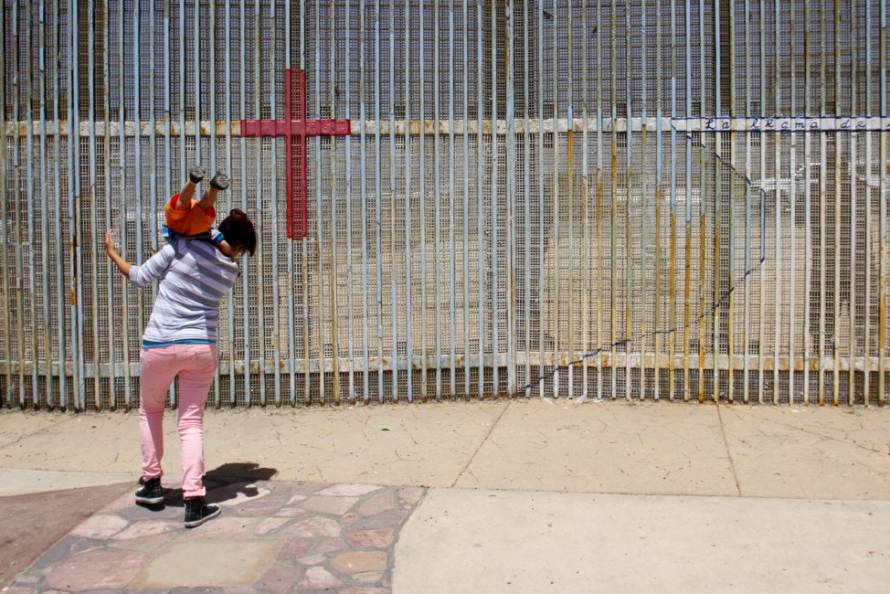 A woman plays with a child by the border fence as they commemorate Mother's Day on the Mexican side of the US-Mexico border in Tijuana