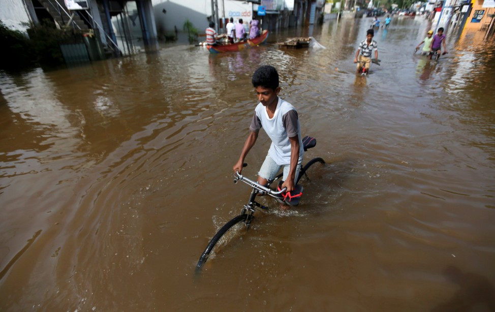 A boy rides his bike along a flooded road in Nagoda village, in Kalutara