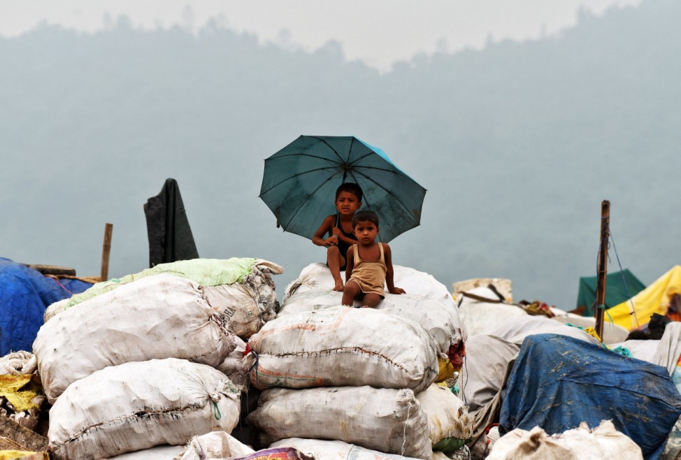 Children shelter under an umbrella during rain as they sit on sacks filled with recyclable material at a garbage dumping site on the eve of World Environment Day, in Guwahati