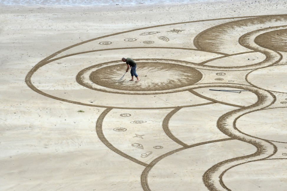Sand artist Marc Treanor creates a work on the North Beach at Tenby Harbour, Pembrokeshire, Wales